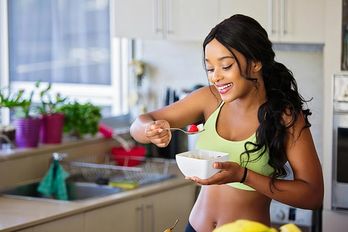 A woman in the kitchen, eating salad from a bowl