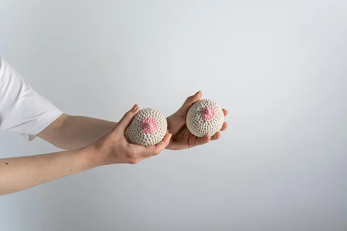 A person holding a knitted breast in beige and pink colours.