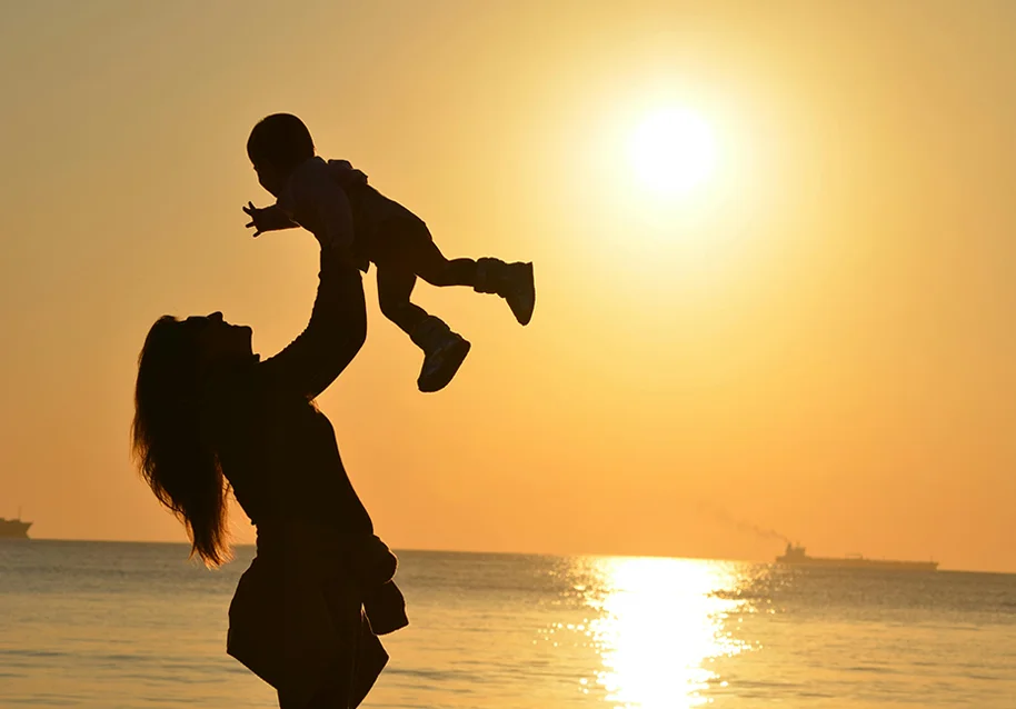 Silhouette of a mother carrying her baby at the beach during golden hour