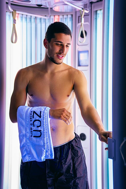 Young man stepping out of a tanning booth, highlighting his toned physique.