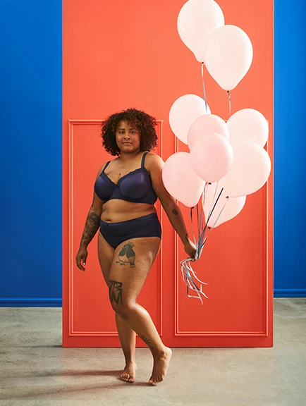 A confident woman with balloons standing in a colourful doorway, promoting body positivity.