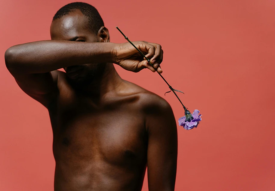 A person holding a flower while covering their face with their hand