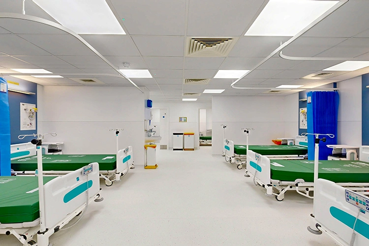 Day surgery recovery ward at London Private Hospital with multiple adjustable beds, blue privacy curtains and bright clinical lighting.