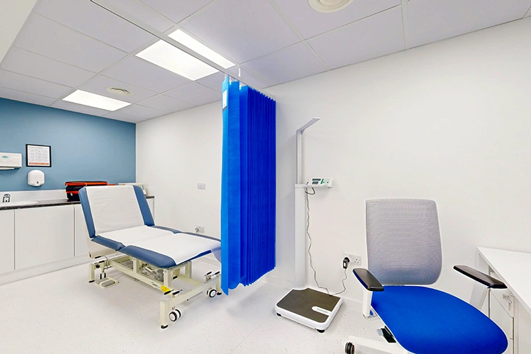 Clinical consultation room at London Private Hospital with adjustable exam couch, blue privacy curtain, digital height/weight scale and patient chair.