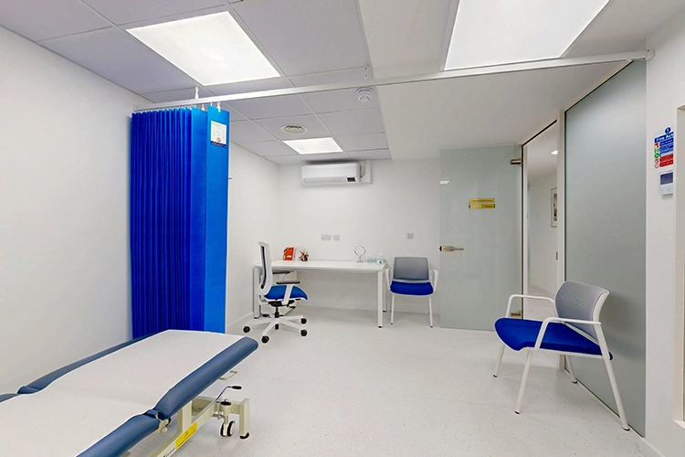 Clinical consultation room at London Private Hospital with adjustable exam couch, blue privacy curtain