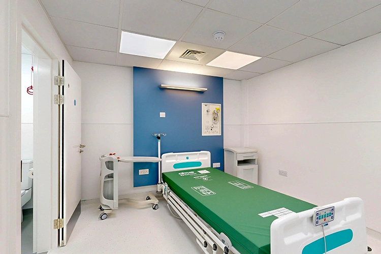 Private patient recovery room at London Private Hospital with adjustable bed, blue feature wall, bedside trolley and en-suite bathroom.